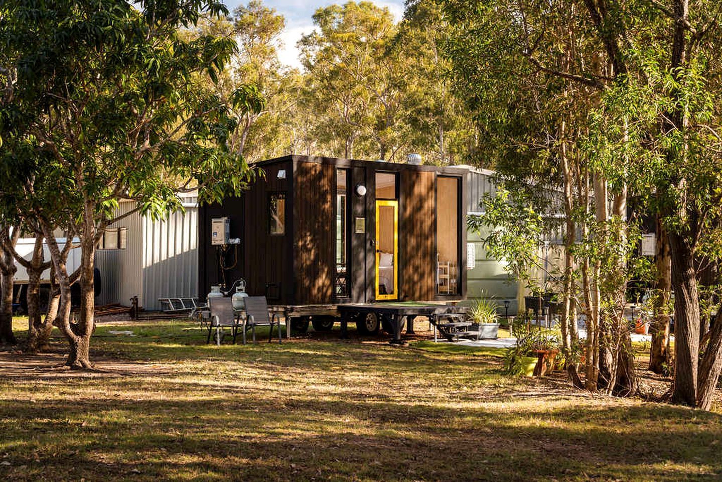 A mobile home with a small deck and outdoor seating area, surrounded by trees.