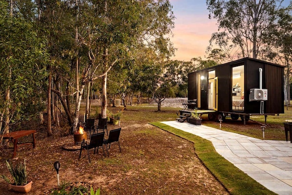 A small, dark-colored cabin with a patio area, outdoor seating, and a fire pit.