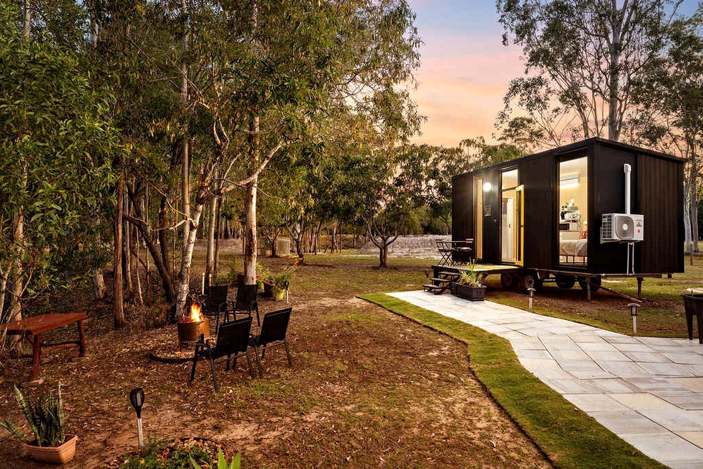 Une petite cabane aux couleurs sombres, dotée d’un patio, de sièges extérieurs et d’un foyer.
