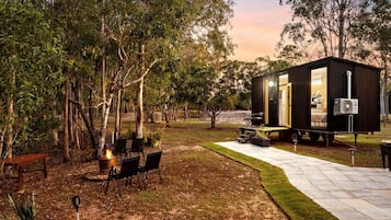 Une petite cabane aux couleurs sombres, dotée d’un patio, de sièges extérieurs et d’un foyer.