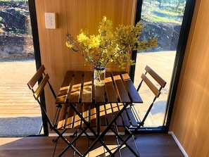 A wooden table with a vase of yellow flowers, a bench, and a view of a natural landscape through a glass door.
