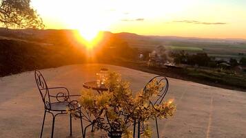 An outdoor seating area with a table and chairs, a vase with a plant, and a scenic view of the sunset over a landscape.