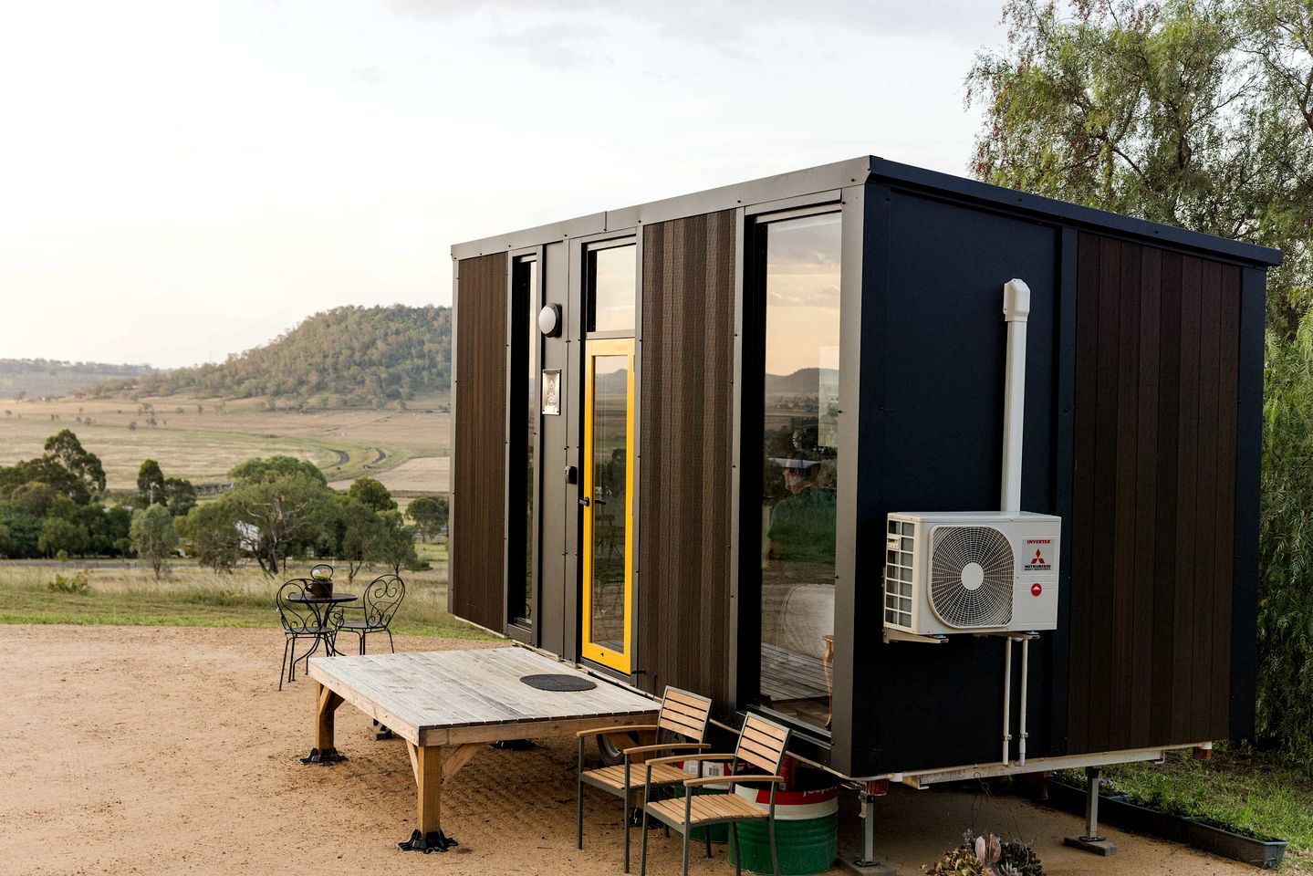 Une structure moderne et compacte dotée d’une grande porte coulissante, d’un petit espace extérieur aménagé pour s’asseoir et d’un appareil de climatisation.