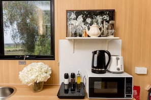 A kitchenette with a microwave, kettle, toaster, and a tank water sign.