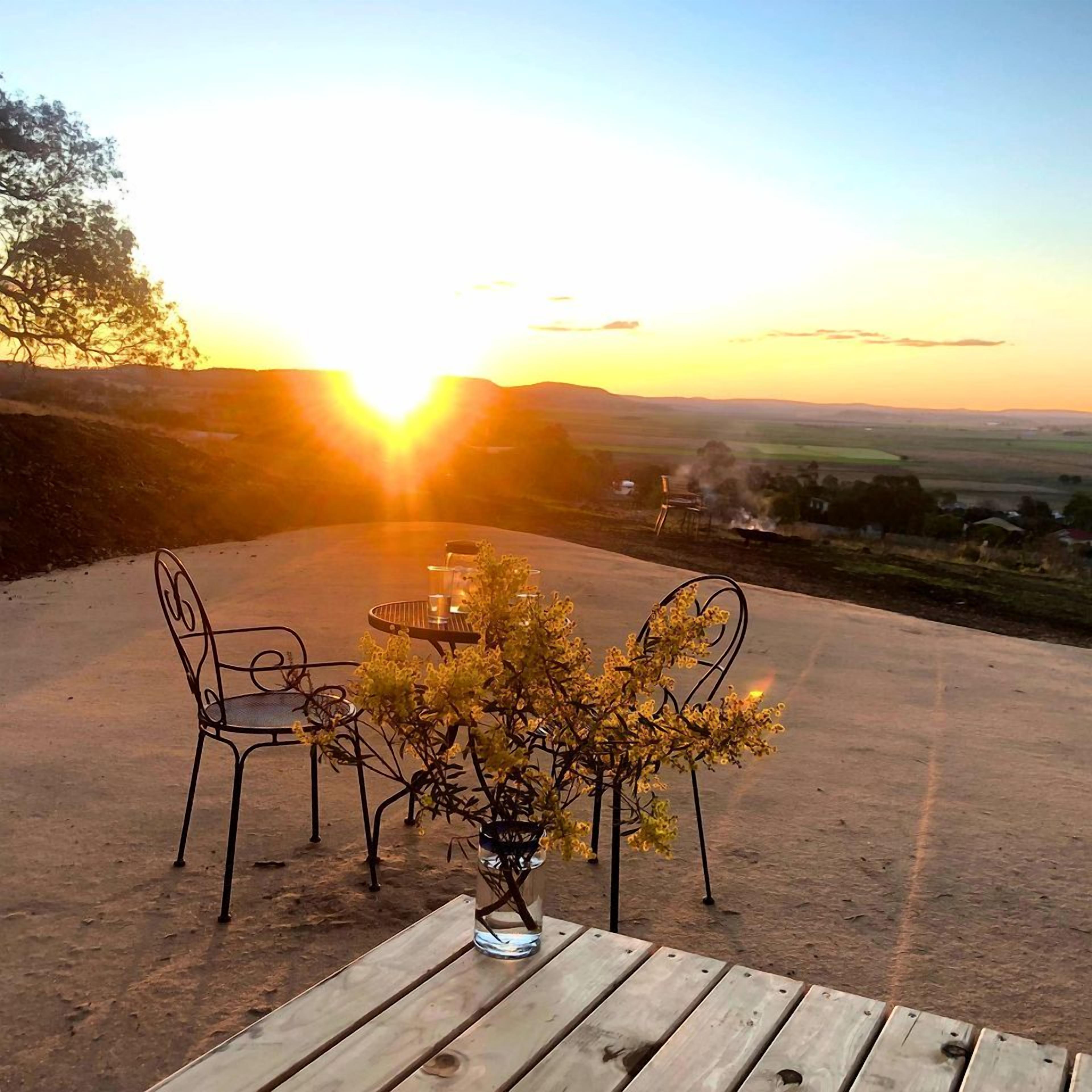 An outdoor seating area with a table and chairs, a vase with a plant, and a scenic view of the sunset over a landscape.