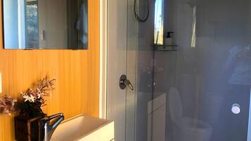 A bathroom with a glass shower enclosure, a white sink, and a wooden vanity.