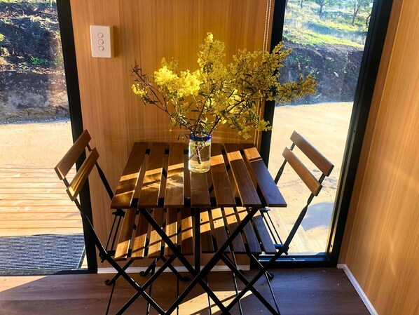 A wooden table with a vase of yellow flowers, a bench, and a view of a natural landscape through a glass door.