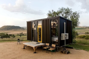 A compact cabin with a wooden deck, a single bed, and a small seating area.
