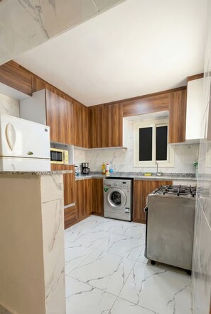 A compact kitchen with wooden cabinets, a built-in microwave, a washing machine, and a gas stove. - 2BRs Hasan Alma'moon Fabulous Apartment (Cairo Governorate)
