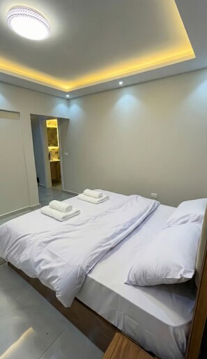 A hotel room with a bed, a bathroom visible through an open door, and a ceiling light fixture. - 2BRs Hasan Alma'moon Fabulous Apartment (Cairo Governorate)