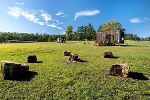 A modern cabin with a large deck area, surrounded by a grassy field with several large rocks.