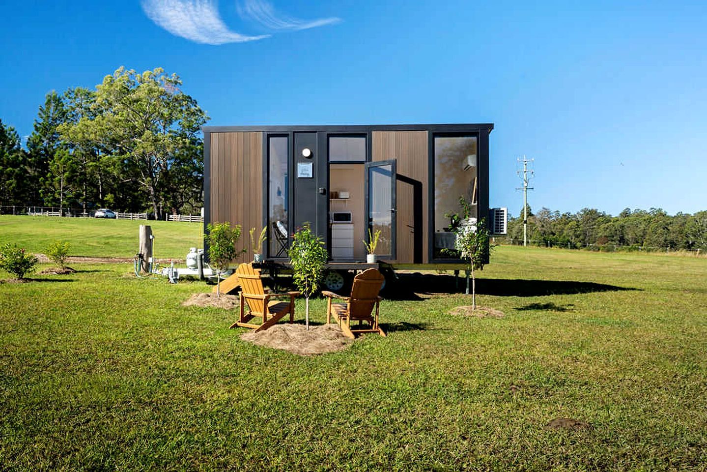 Une maison mobile moderne dotée d’une grande porte coulissante, d’un petit patio avec deux chaises et d’une pelouse en arrière-plan.