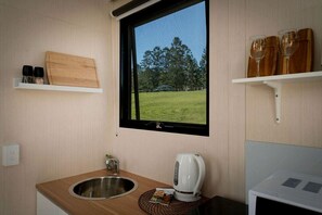 A compact kitchen with a window, a sink, a kettle, and a microwave.