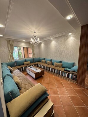 A living room with a sectional sofa, a coffee table, and a chandelier. - Immiouadar Elegant apartment piscine, 2min/beach (AGADIR)