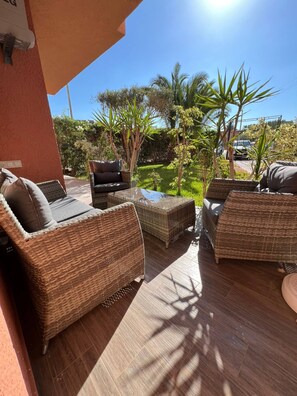 An outdoor patio area with wicker furniture and a view of a garden. - Immiouadar Elegant apartment piscine, 2min/beach (AGADIR)
