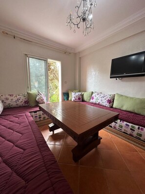 A living room with a sofa set, a wooden coffee table, a TV mounted on the wall, and a chandelier. - Immiouadar Elegant apartment piscine, 2min/beach (AGADIR)