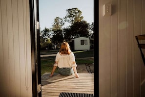 A person sitting on a wooden deck with a view of a small house and trees in the background.