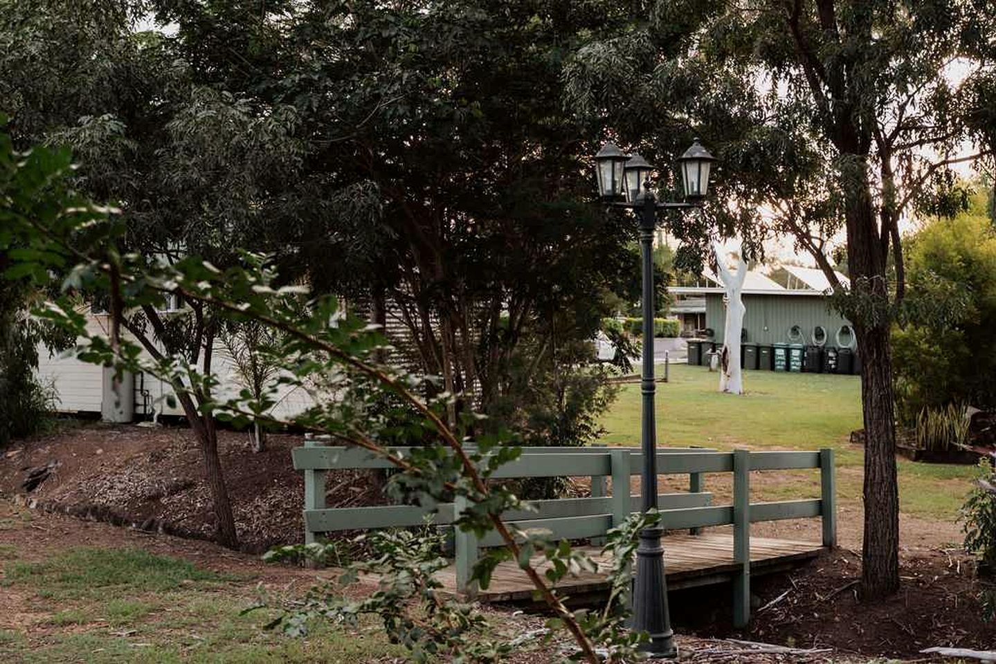A park area with a wooden bench, a lamp post, and a building in the background.