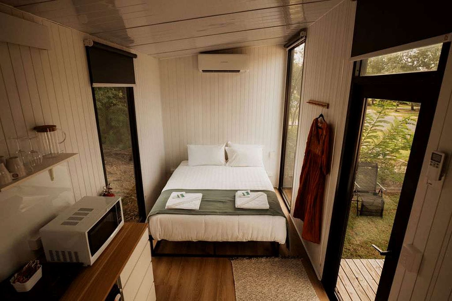 A compact bedroom with a bed, a microwave, and a window.