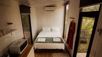 A compact bedroom with a bed, a microwave, and a window.