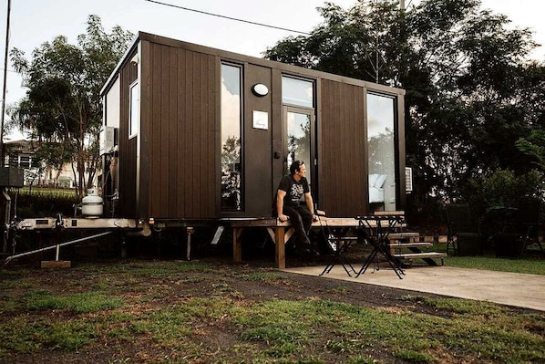 A modern, compact mobile home with a flat roof, large windows, and a small porch area.