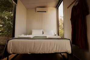 A bedroom with a bed, pillows, a blanket, and an air conditioning unit.