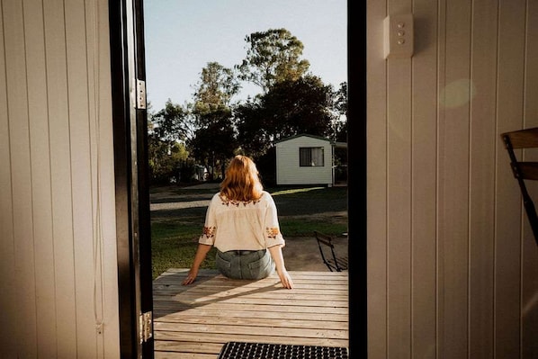 A person sitting on a wooden deck with a view of a small house and trees in the background.