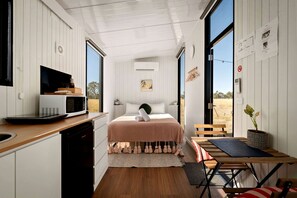 A compact bedroom with a bed, bedside table, and a view of the outdoors.