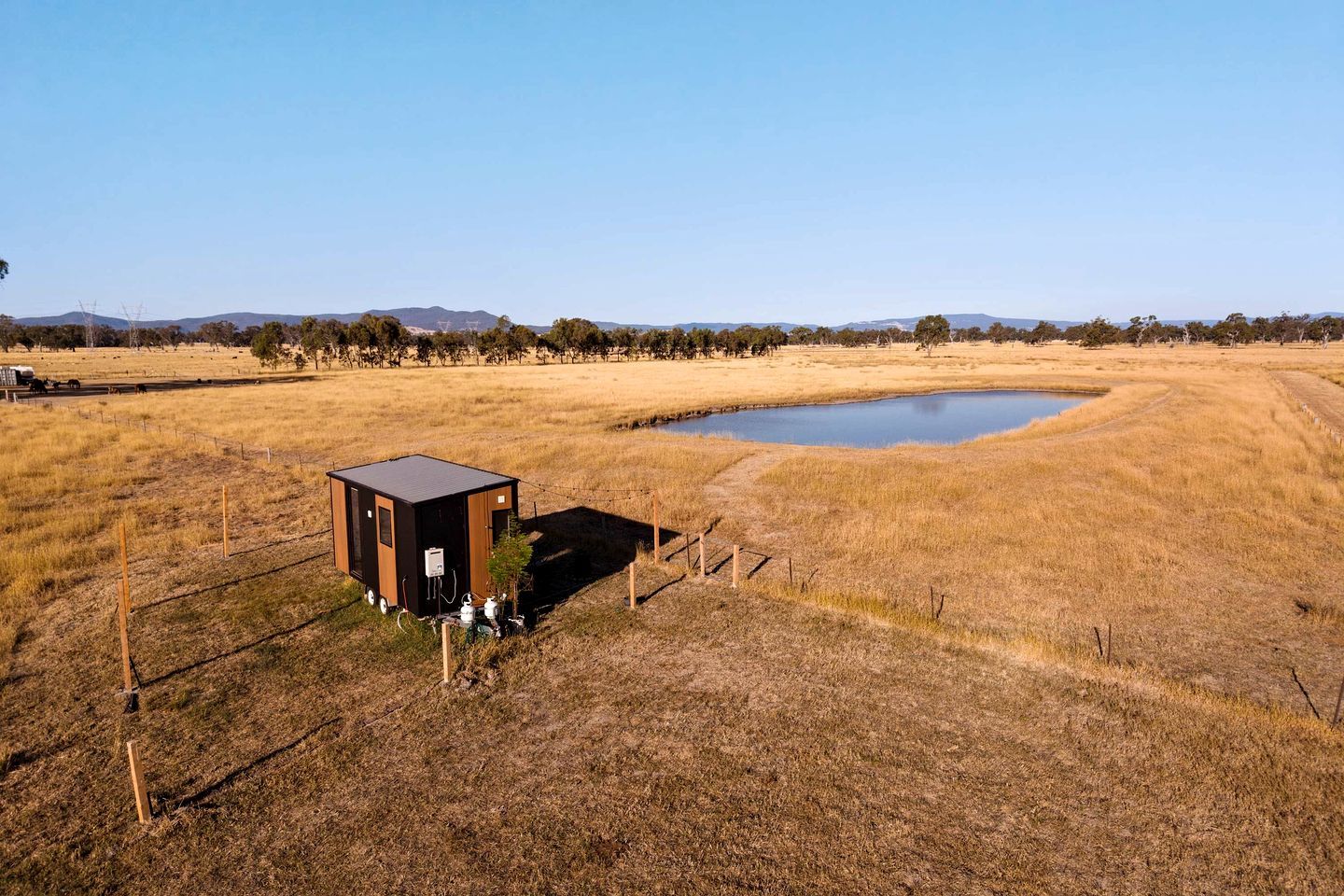 A small, single-story building with a flat roof, situated in a dry grass field with a body of water nearby.