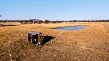 A small, single-story building with a flat roof, situated in a dry grass field with a body of water nearby.