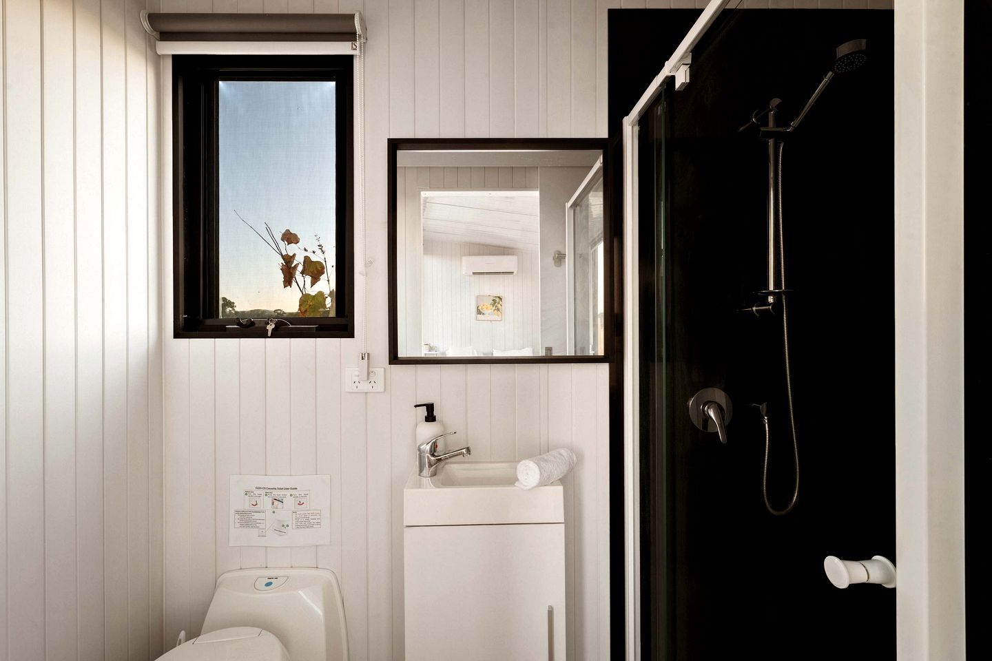 A bathroom with a toilet, sink, mirror, and shower.