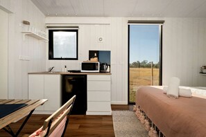 A compact bedroom with a bed, a small desk with a microwave, a window, and a view of the outdoors.