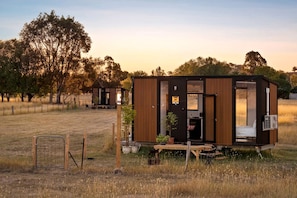A small cabin with a door and windows, situated in a grassy field with trees in the background. - Cozy Tiny House with Firepit Under Starry Skies in Maindample, Australia (Maindample)