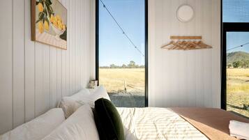 A bedroom with a bed, a window with a view of a field, and a painting of lemons on the wall.