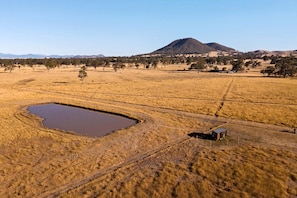A rural landscape with a small building near a water body and a hill in the background.