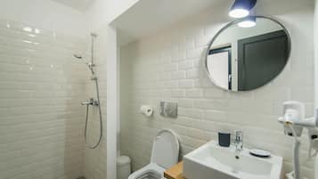 A bathroom with white tiled walls, a shower, a toilet, and a sink with a mirror above it.