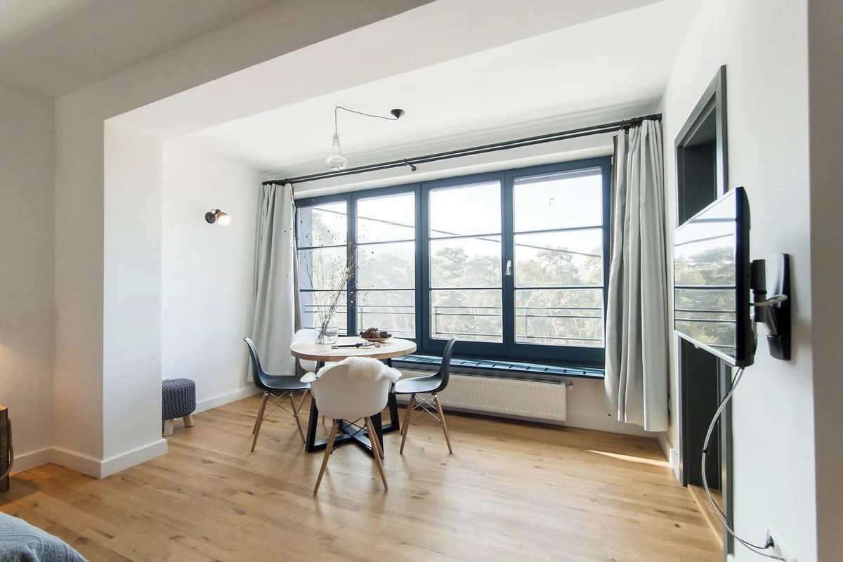 A modern room with a large window, a dining table with chairs, and a flat-screen TV mounted on the wall.