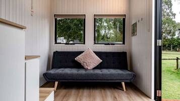 Een modern interieur met een donkergrijze bank, twee ramen en een houten vloer.