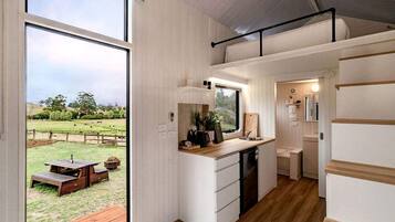 A compact kitchen with a window, a sink, and a small dining area visible through the window.