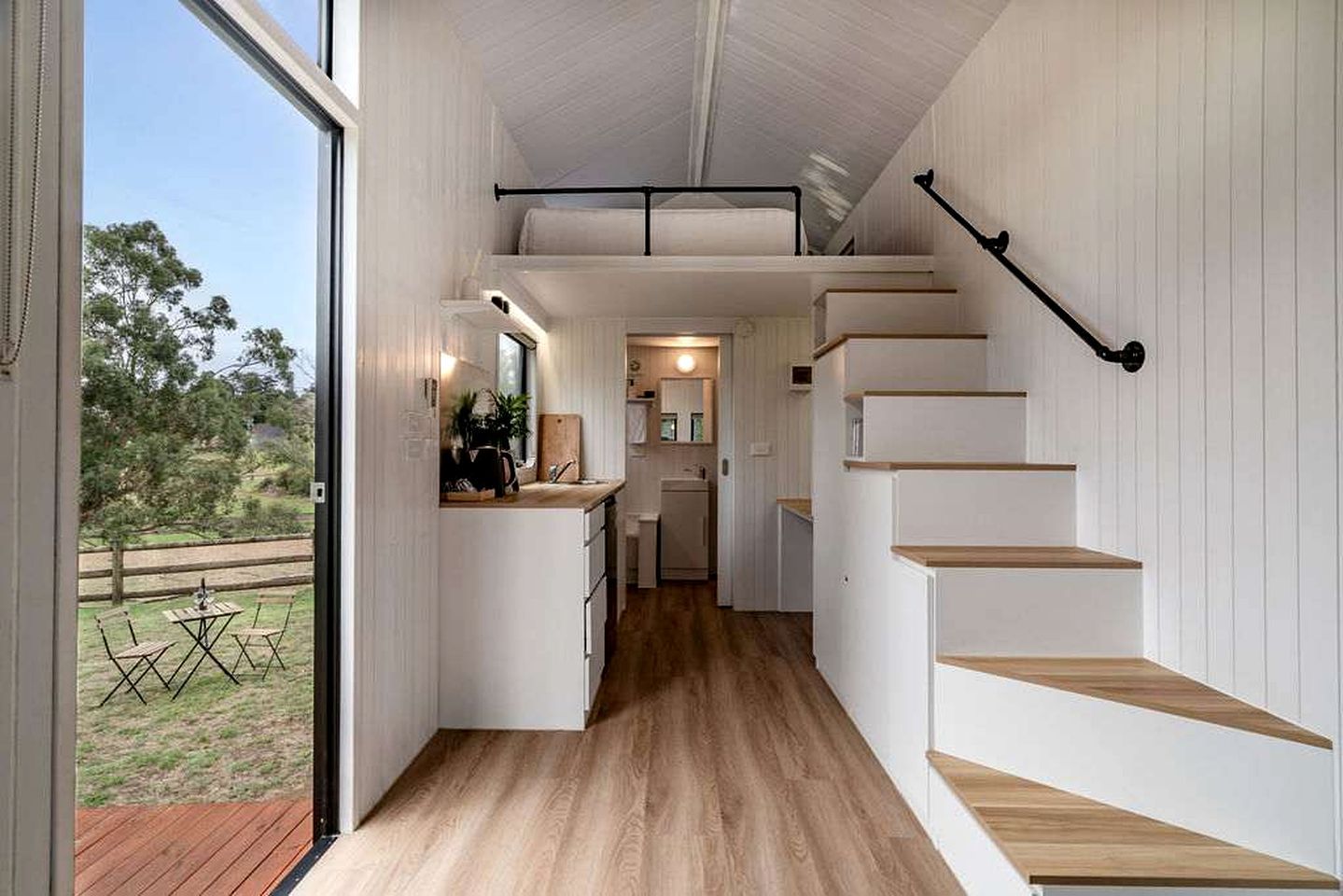 Um interior moderno com área de cozinha, piso de madeira e escada.