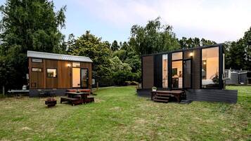 Duas cabanas modernas com grandes janelas, decks de madeira e áreas de estar ao ar livre.