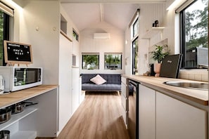 A compact kitchen with a microwave, sink, and a sofa in the background.