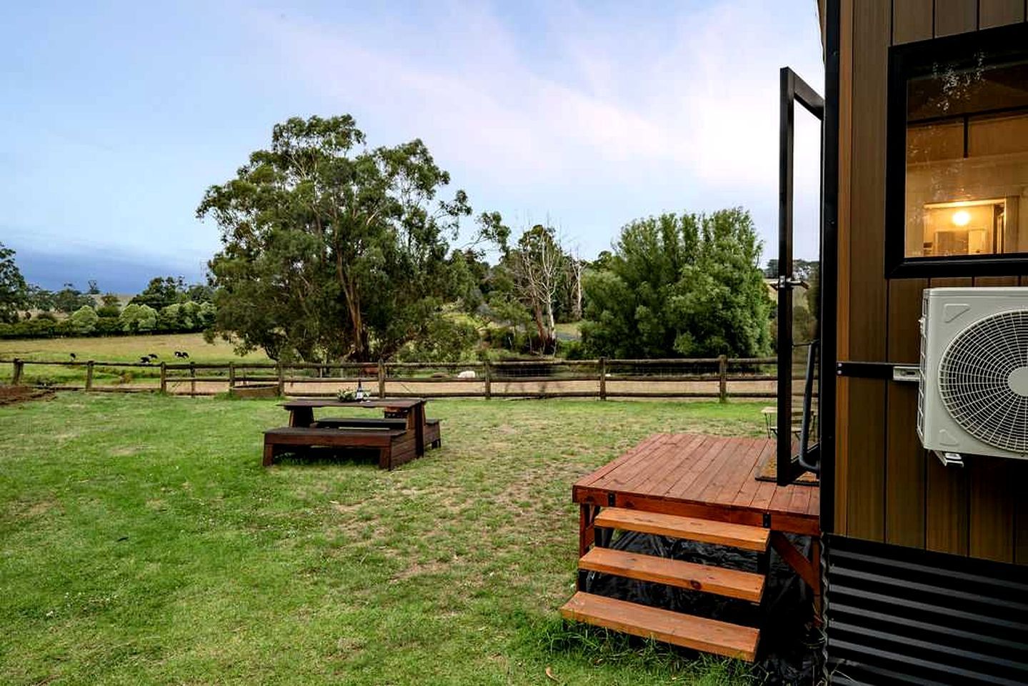 Área de varanda externa com deck de madeira, mesa de piquenique e um ventilador grande.