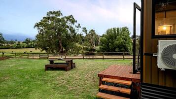 Área de varanda externa com deck de madeira, mesa de piquenique e um ventilador grande.