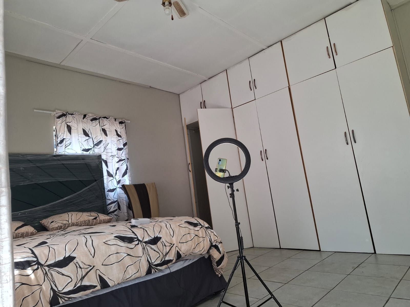 A bedroom with a bed, a wardrobe, a ring light, and a curtain with a leaf pattern.