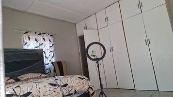 A bedroom with a bed, a wardrobe, a ring light, and a curtain with a leaf pattern.