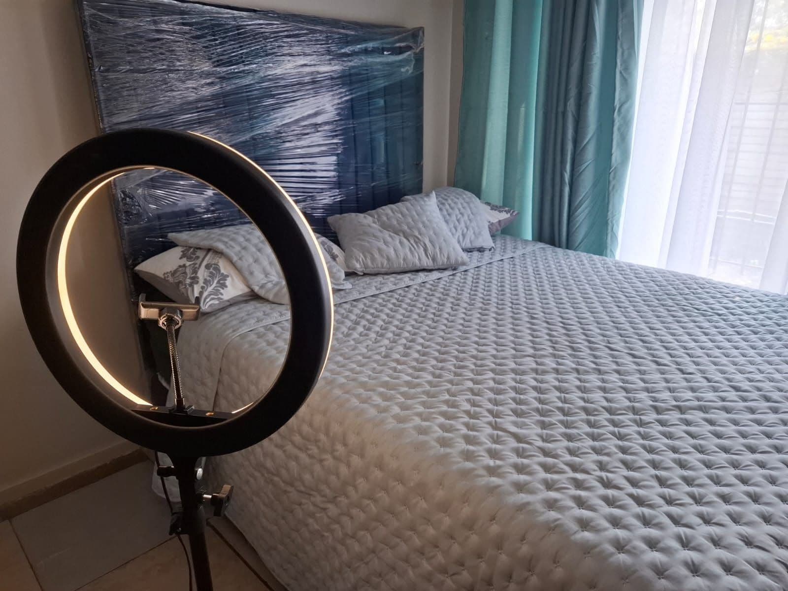 A bedroom with a bed, a headboard, and a ring light.
