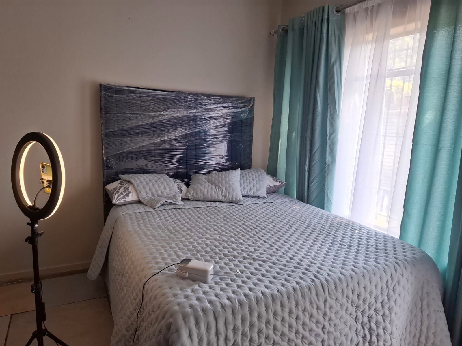 Une chambre à coucher avec un lit, une table de chevet, un miroir et une fenêtre avec des rideaux.