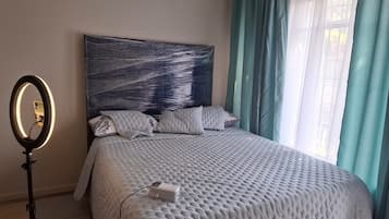 Une chambre à coucher avec un lit, une table de chevet, un miroir et une fenêtre avec des rideaux.