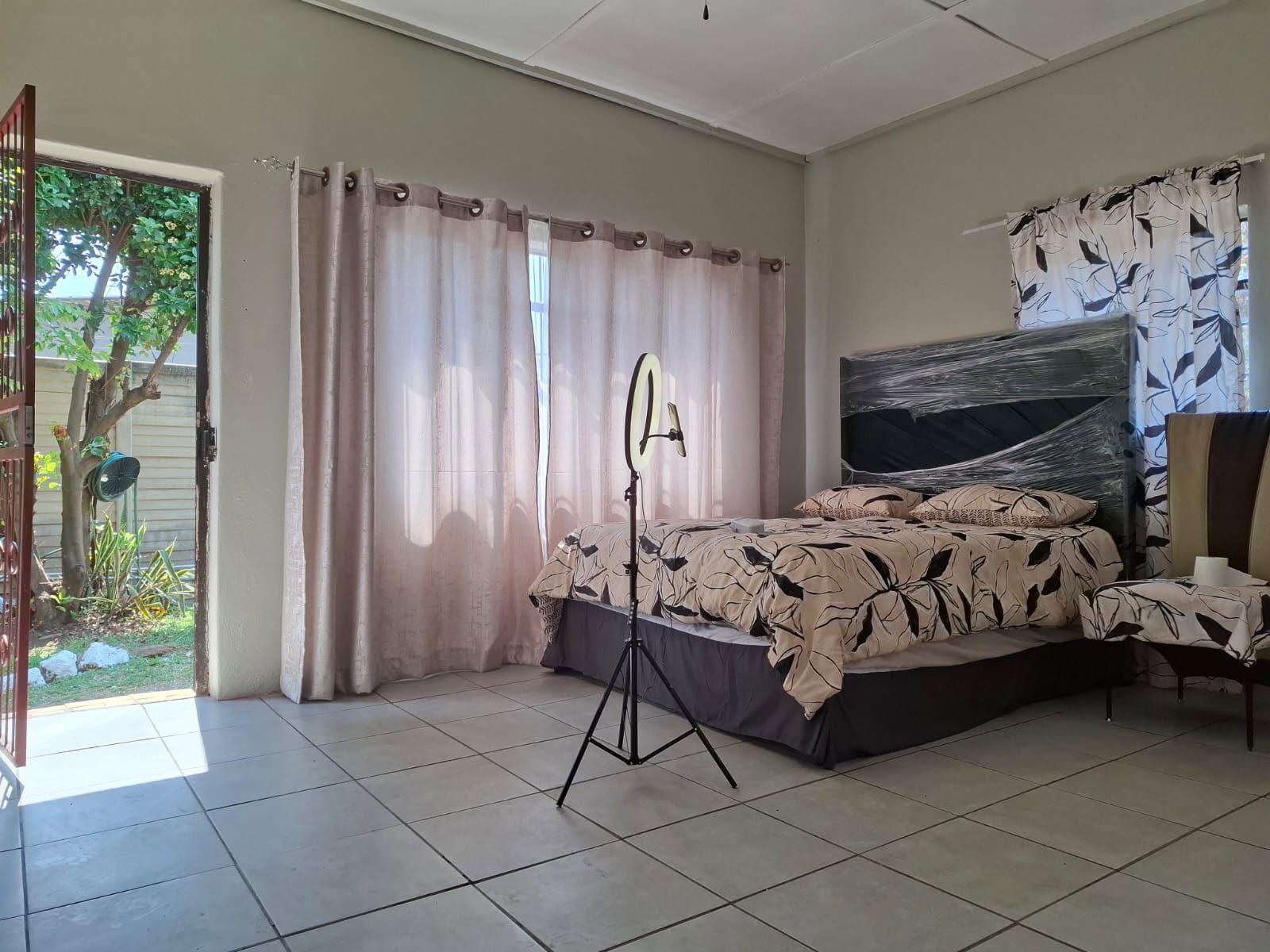 A bedroom with a bed, a standing lamp, and a view of the outside.